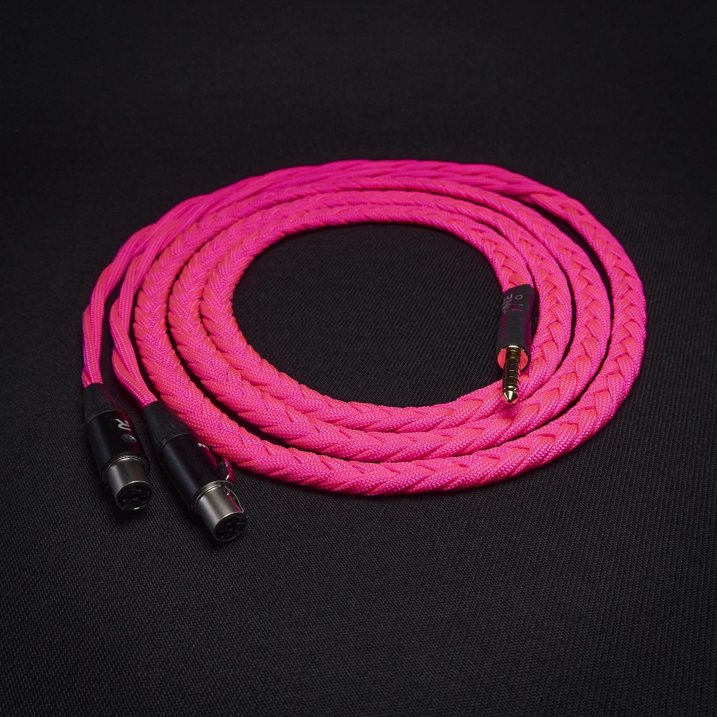 Pink braided audio cable with black connectors on a black background