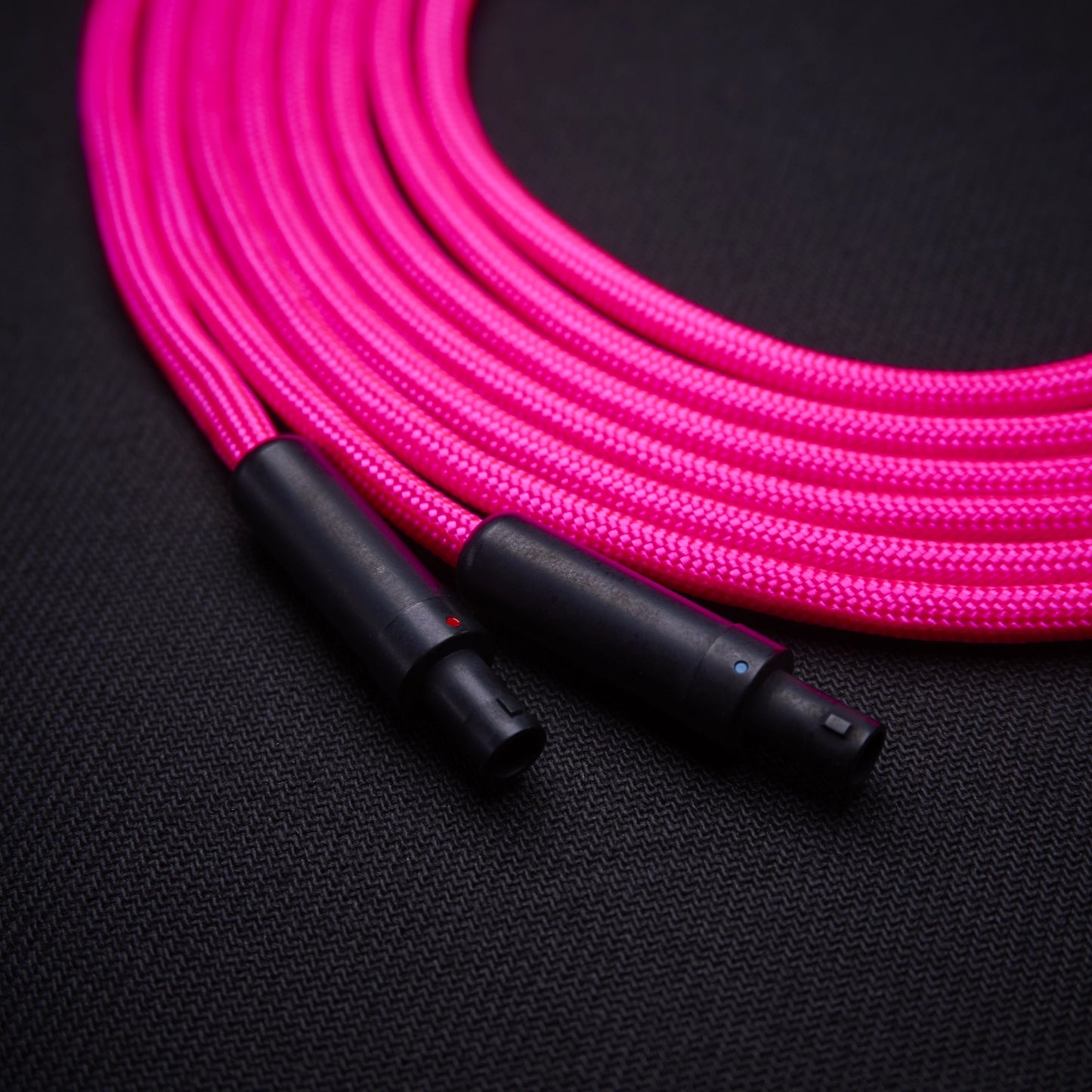 Pink braided cable with black connectors on a dark background