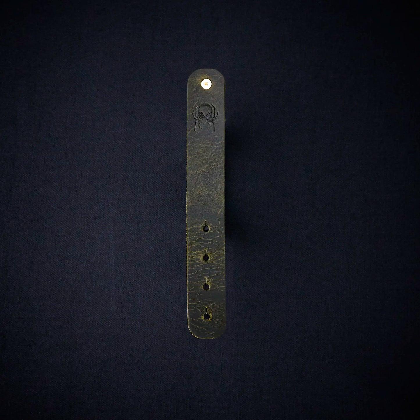 Fermata leather cable organizer in Fir (dark green) with brass stud and embossed Arachne spider
