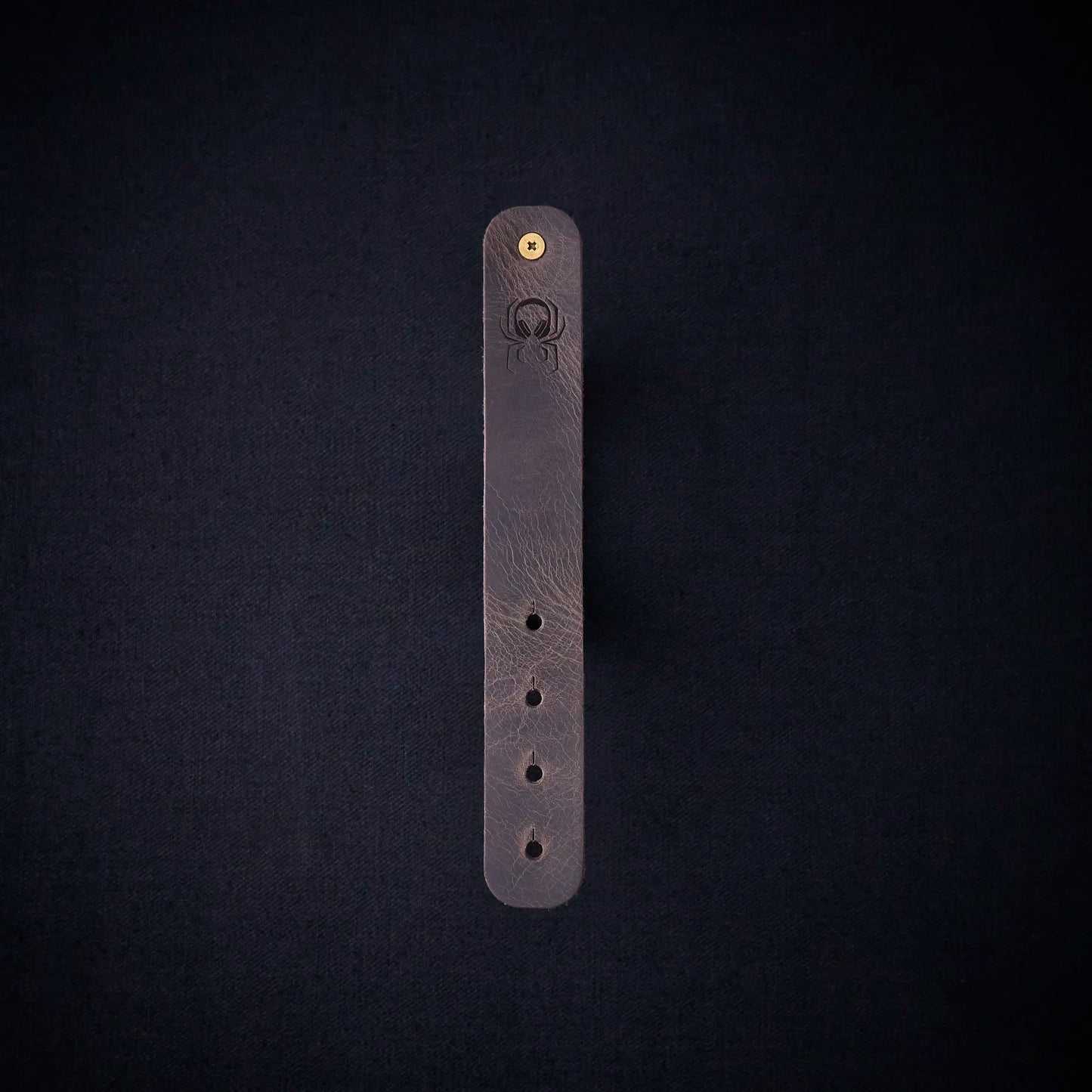 Fermata leather cable organizer in Graphite (grey) with brass stud and embossed Arachne spider
