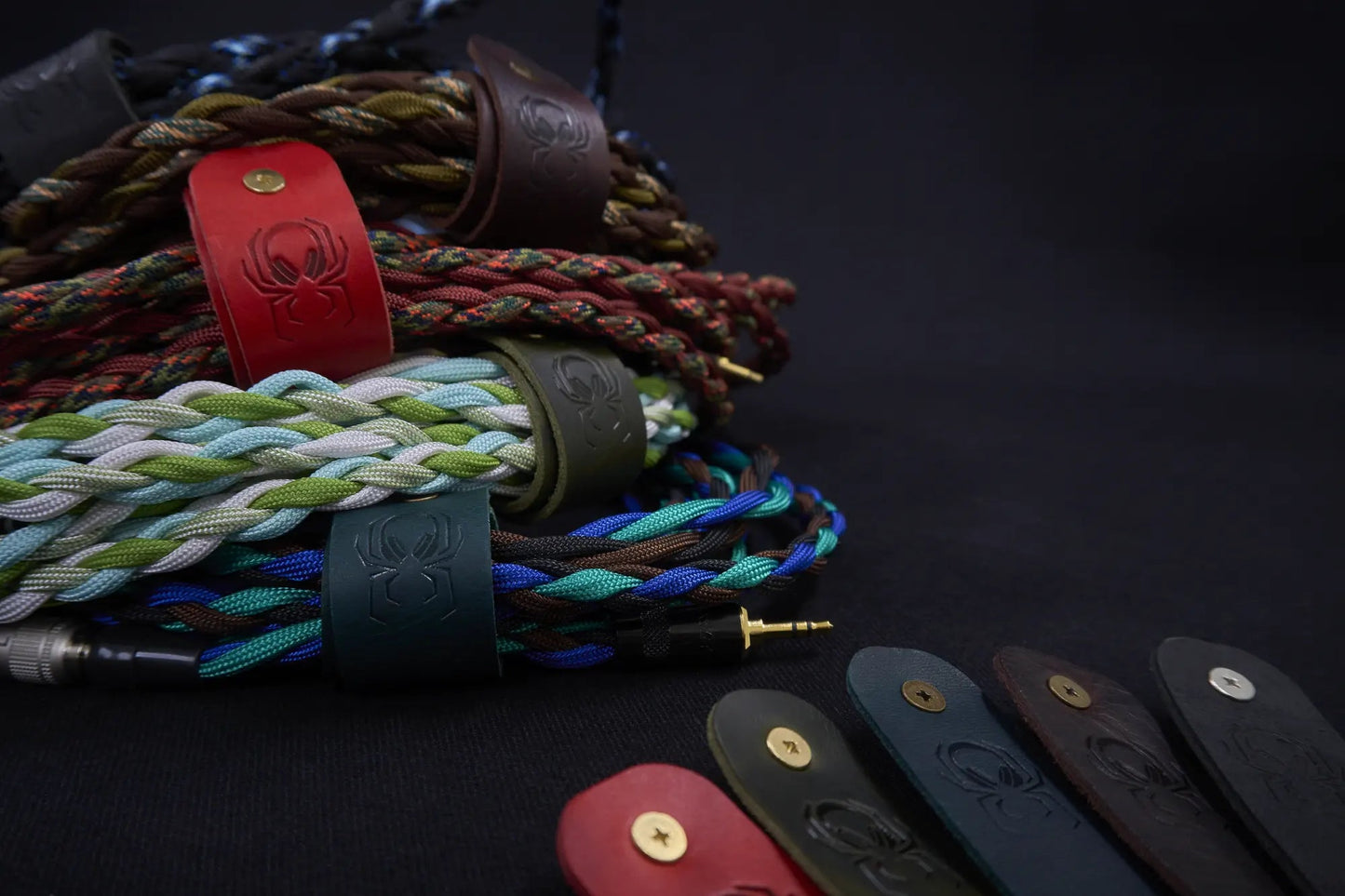 Fermata leather cable keepers wrapped around Arachne Audio braided cables with a brass 3.5mm connector, embossed spider detail.