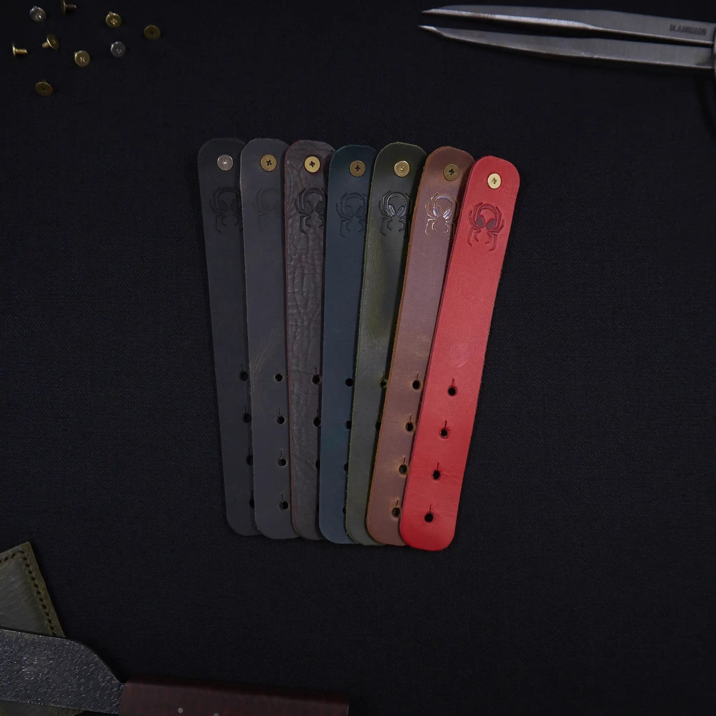 Range of Fermata leather cable straps in seven colours (black, grey, brown, teal, olive, tan, red) with brass studs and embossed Arachne spider, hand-cut in Tallinn.