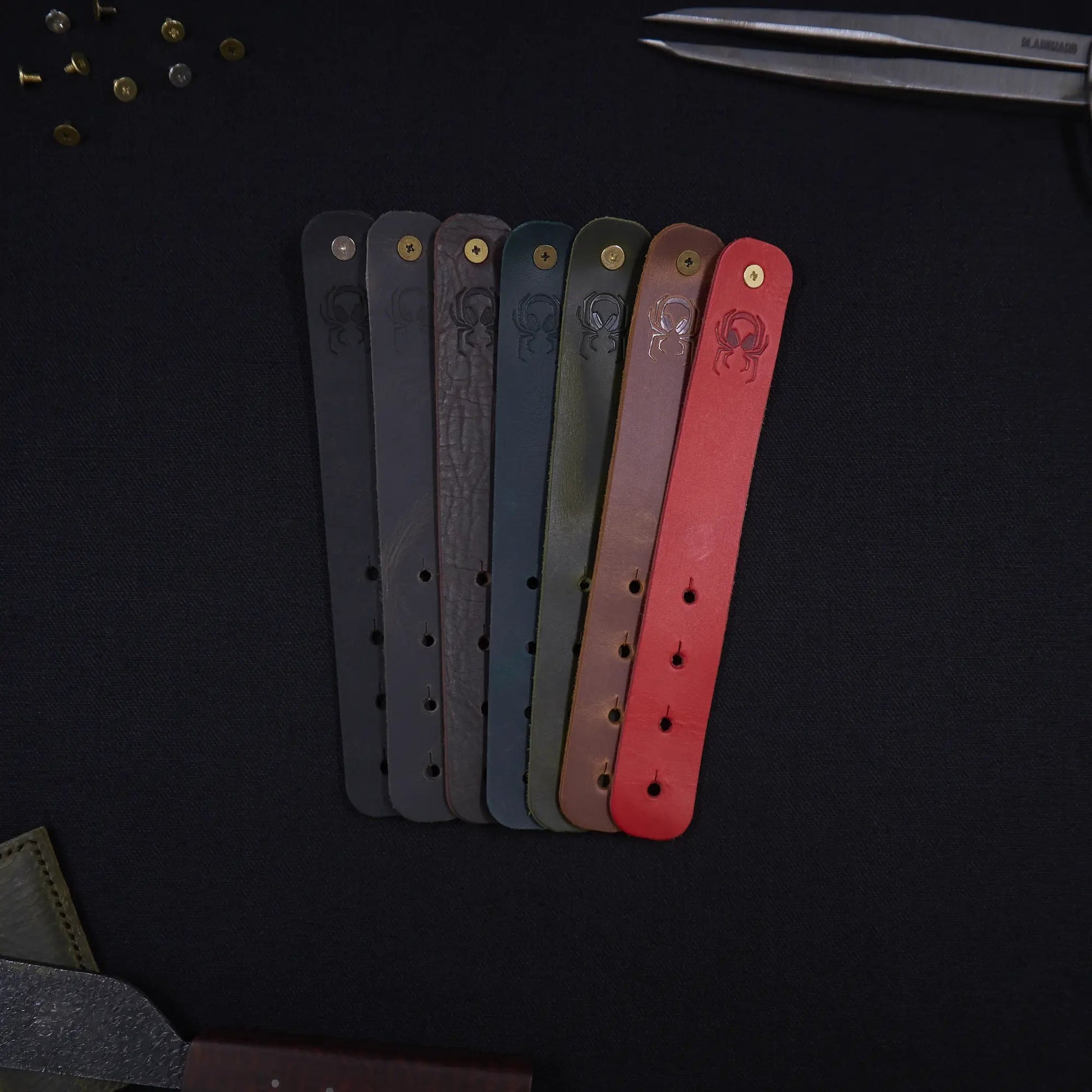 Range of Fermata leather cable straps in seven colours (black, grey, brown, teal, olive, tan, red) with brass studs and embossed Arachne spider, hand-cut in Tallinn.