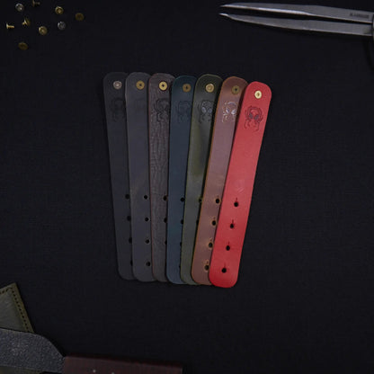 Range of Fermata leather cable straps in seven colours (black, grey, brown, teal, olive, tan, red) with brass studs and embossed Arachne spider, hand-cut in Tallinn.