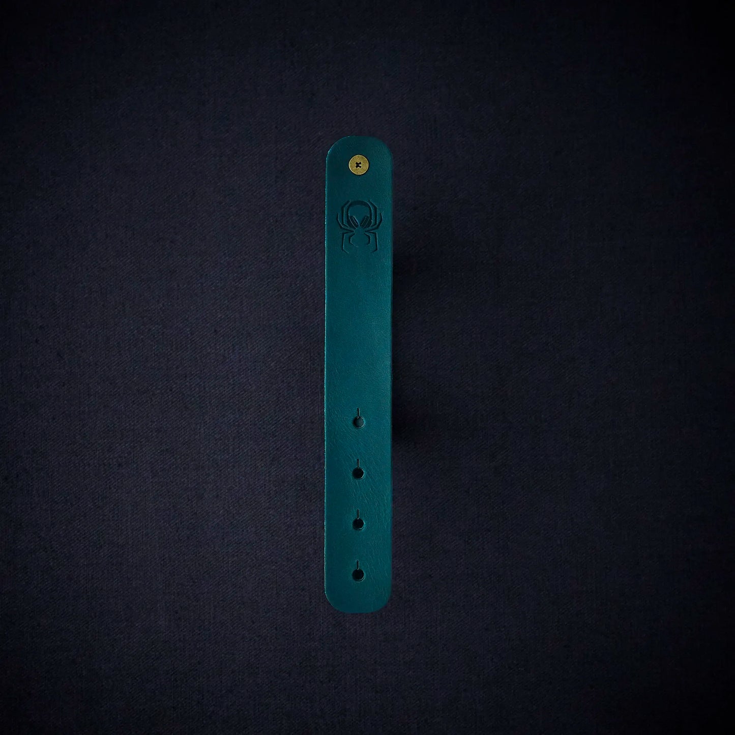 Fermata leather cable organizer in Verdigris (teal) with brass stud and embossed Arachne spider